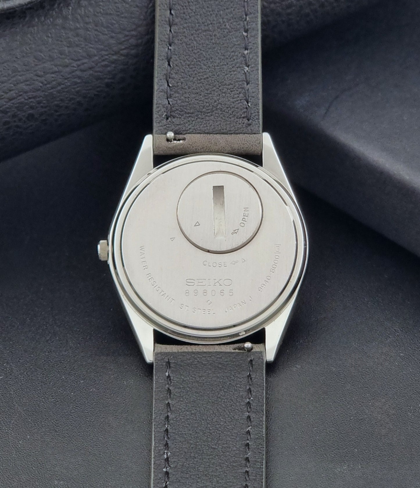 Vintage Seiko Grand Quartz 9940-8000 Watch with gray leather strap and white dial on a dark background case back view