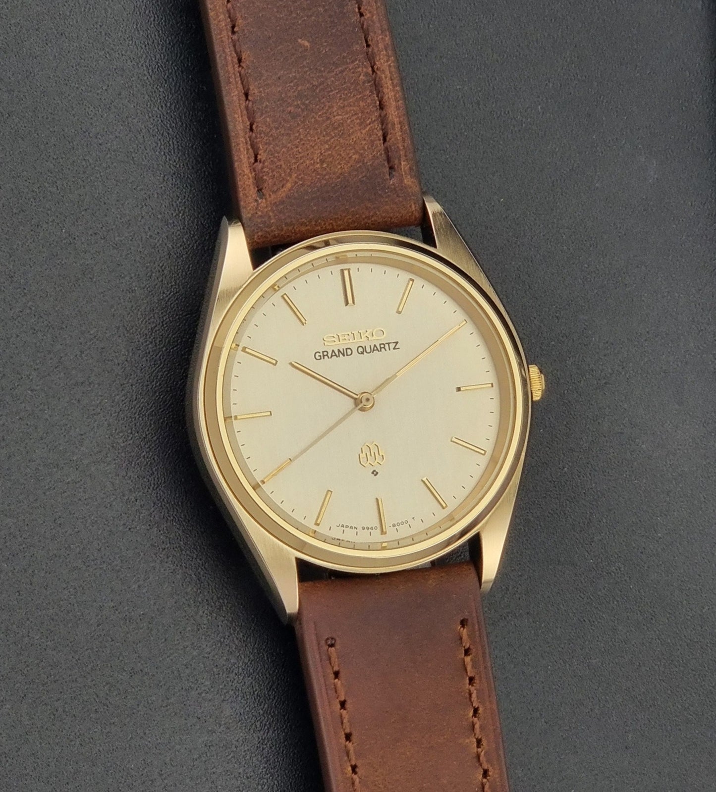 Vintage Seiko Grand Quartz watch 9940-8010 with brown leather strap on a dark textured background front view