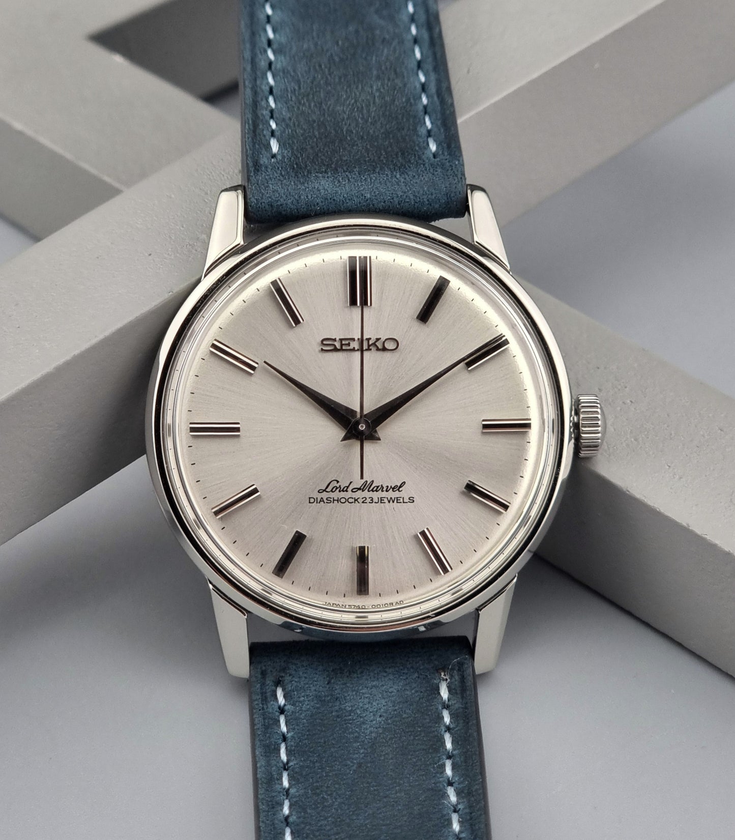 Vintage Seiko Lord Marvel wristwatch with blue leather strap on a geometric gray background