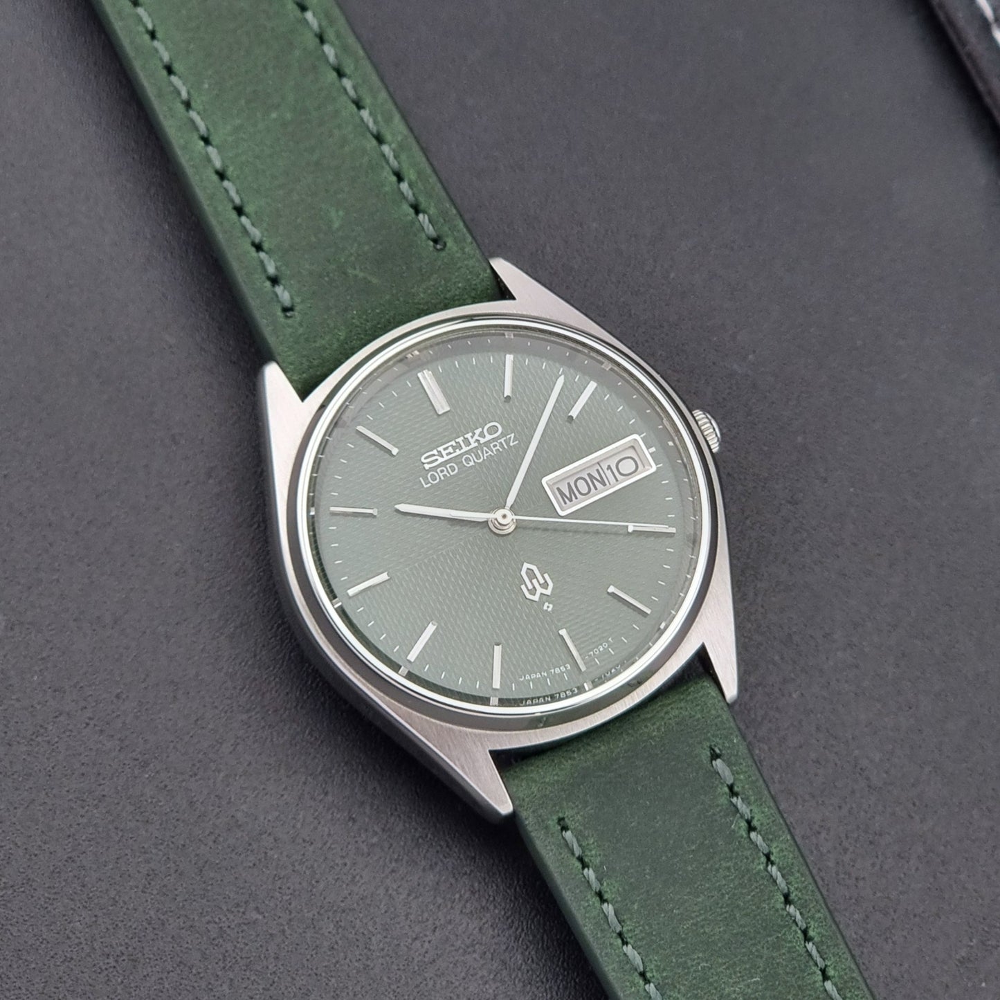 Vintage Seiko Lord Quartz watch 7853-7020 with green strap and silver case on a dark gray background front view