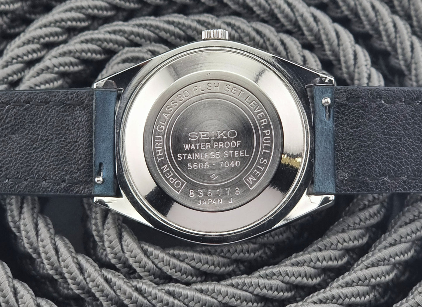 Seiko watch case back with blue strap on a textured gray background