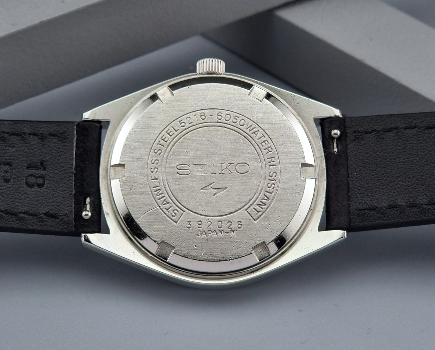 Seiko watch back with black strap on gray background