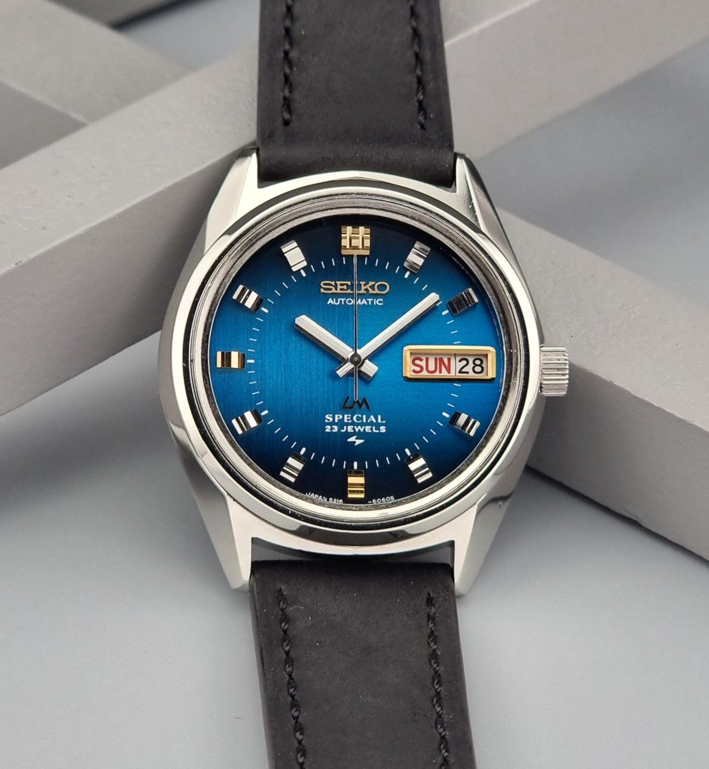 Vintage Seiko Lord Matic watch with blue dial and black leather strap on a gray background
