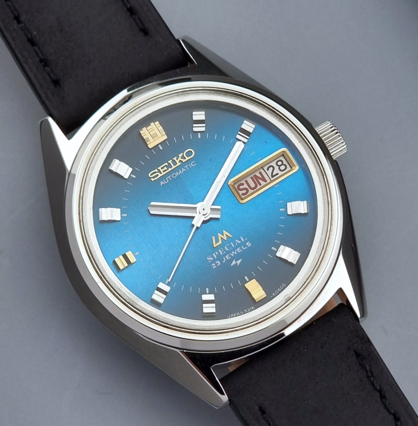 Vintage Seiko Lord Matic watch with blue dial and black leather strap on gray background