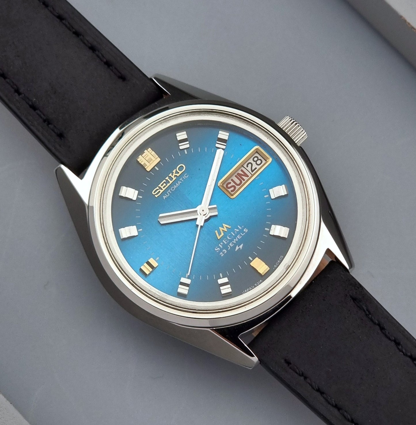 Vintage Seiko Lord Matic watch with blue dial and black leather strap on a gray background