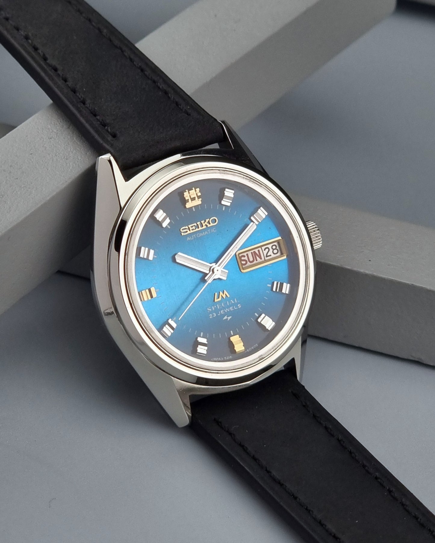 Vintage Seiko Lord Matic watch with blue face and black leather strap on a gray surface