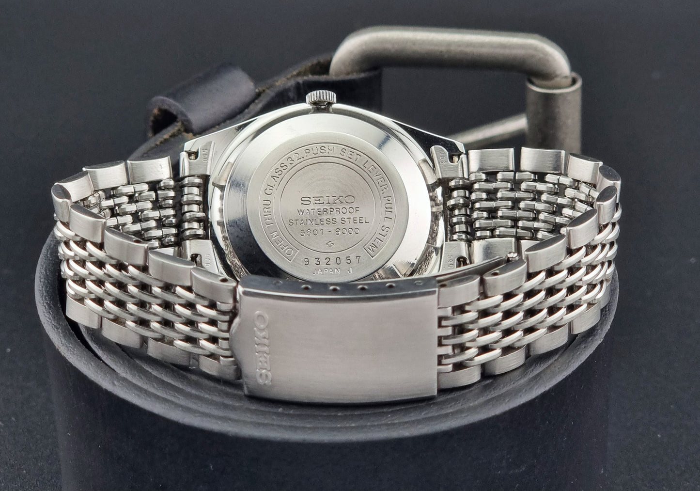 Silver Seiko watch case back with mesh band on a black background