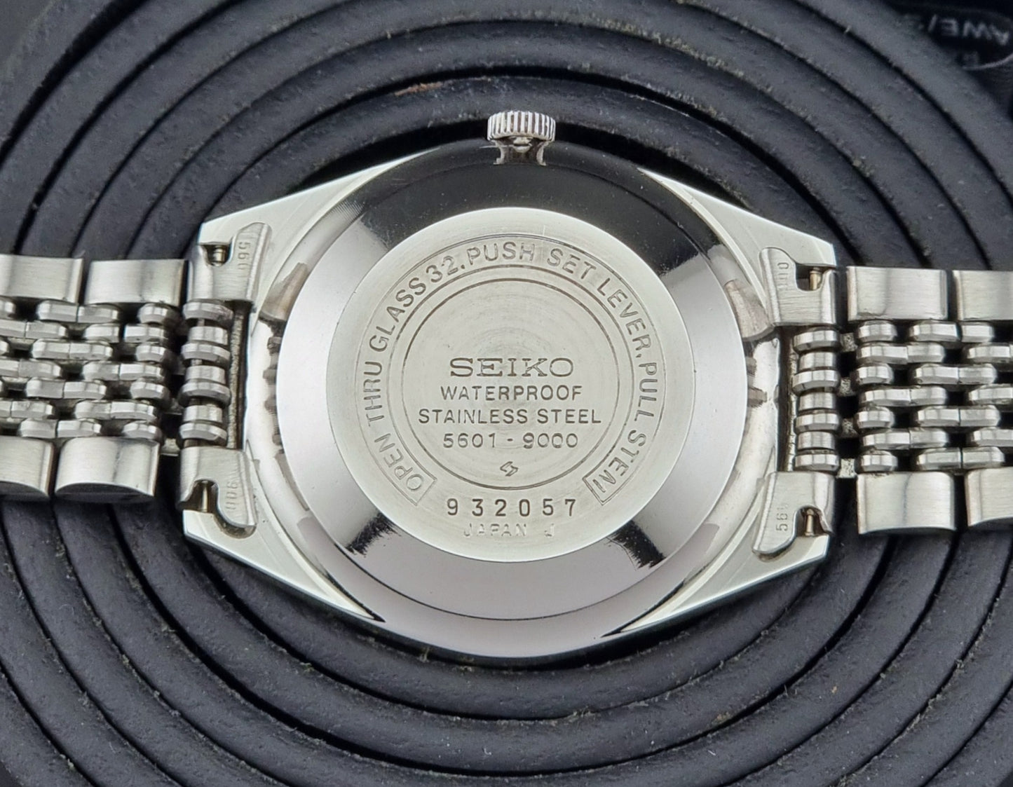Back view of a Seiko Lord Matic watch with metal band on a textured black background