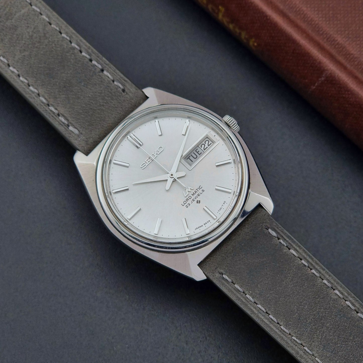 Vintage Seiko Wristwatch LordMatic 5606-7000 with gray leather strap on a dark surface