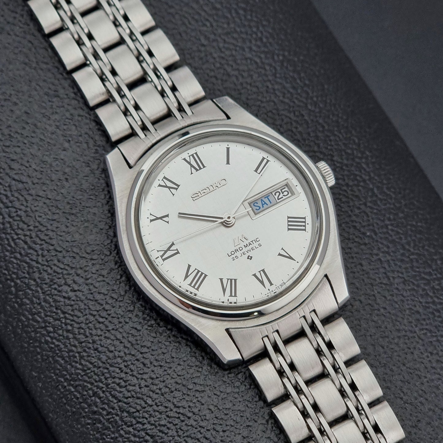 Silver Seiko watch with a metallic band on a dark textured background
