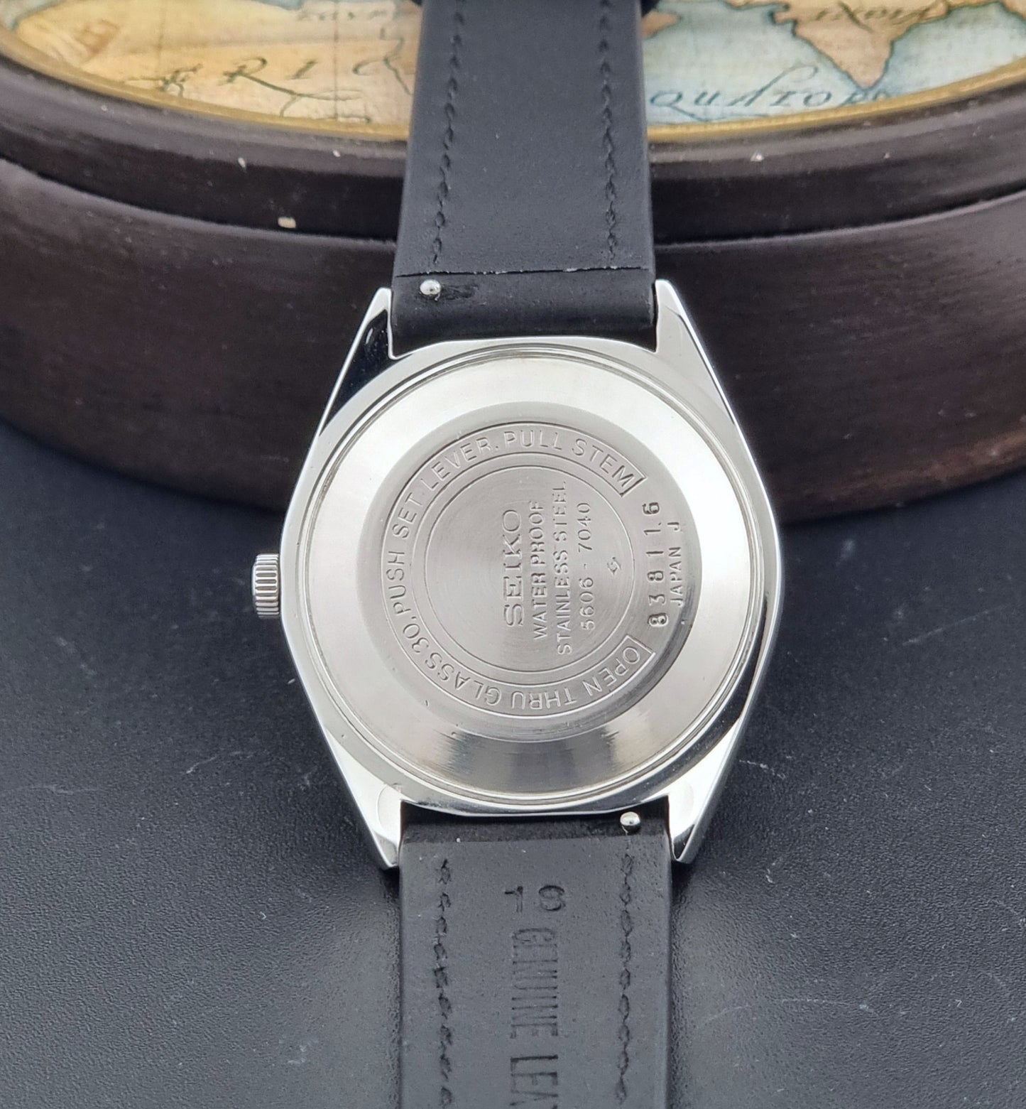 Vintage Seiko Wristwatch LordMatic 5606-7040 with black leather strap on a dark surface case back view