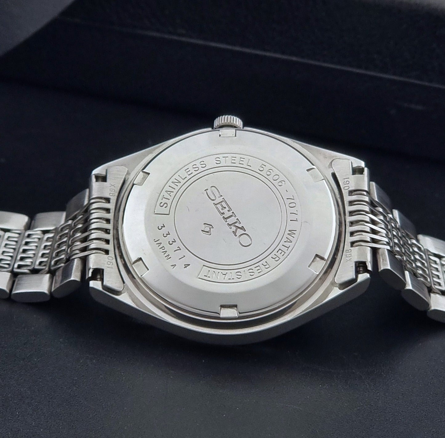 Vintage Seiko Wristwatch 5606-7071 with a metallic band on a dark background case back view