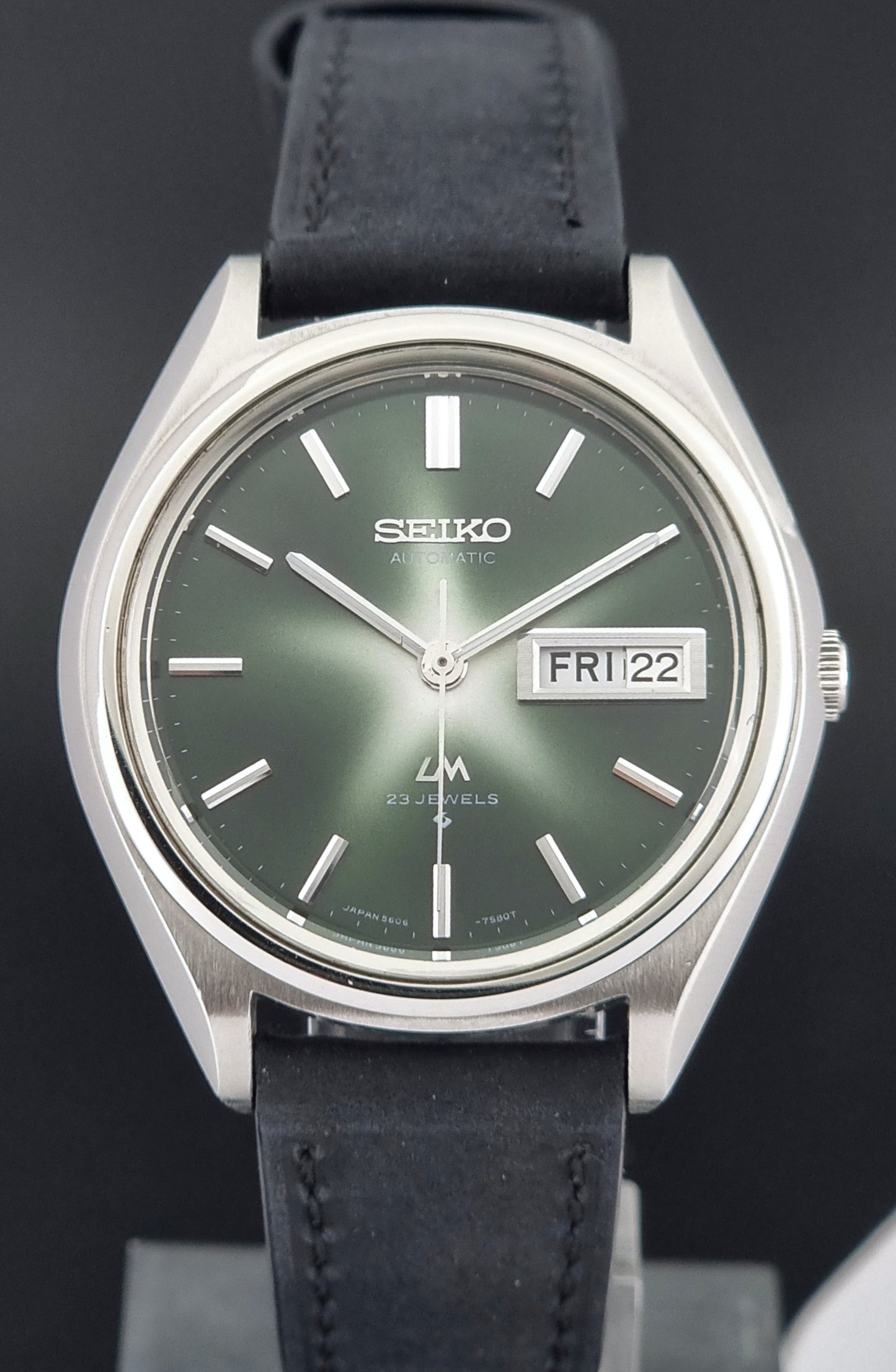 Front view of a Vintage Seiko Lord Matic watch with black leather strap and green dial on a dark background