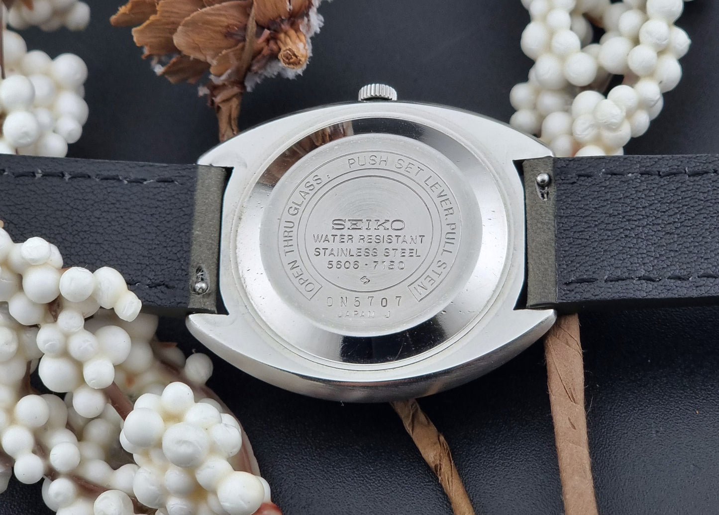 Vintage Seiko Lordmatic 5606-7150 wristwatch with a dark gray strap on a dark background case back view