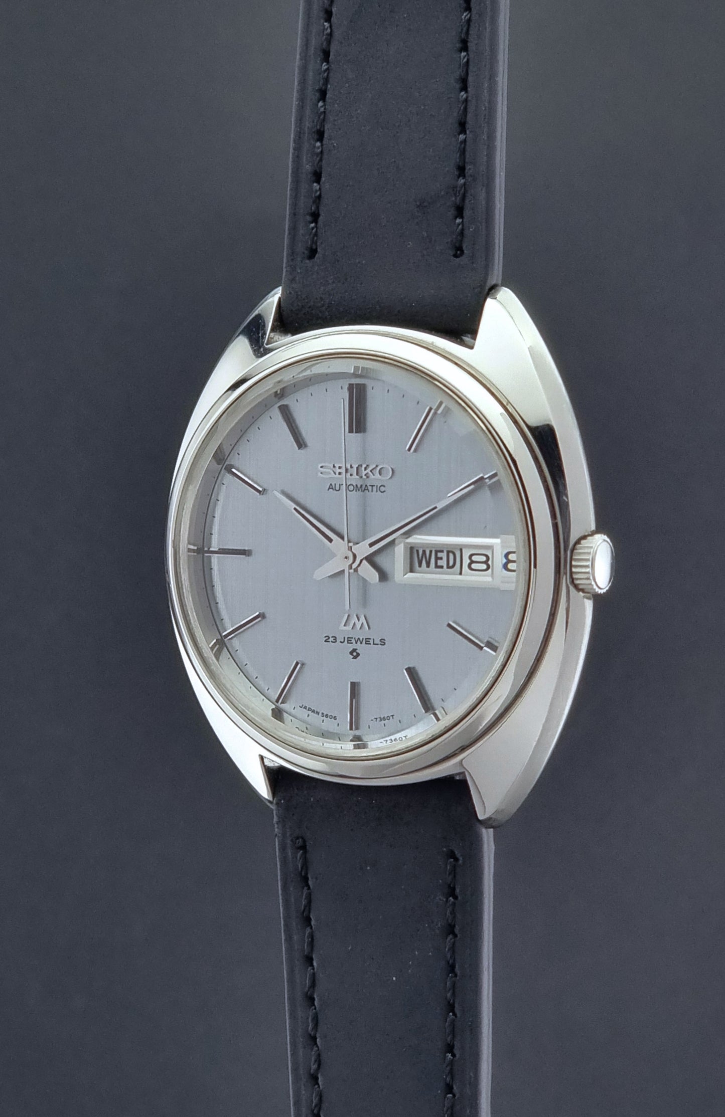 Vintage Seiko Lord Matic 5606-7150 watch with black leather strap on a dark background crown profile view