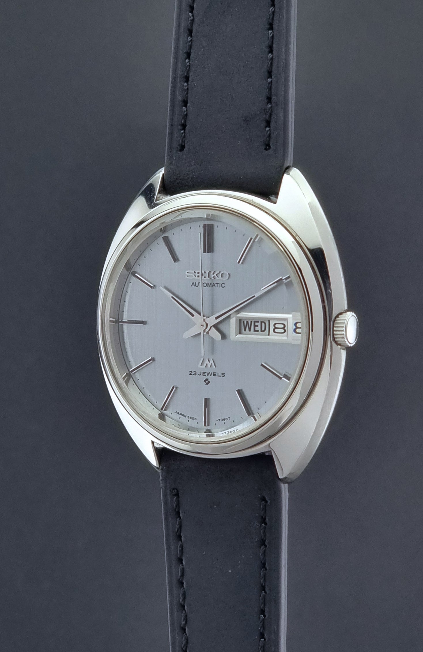 Vintage Seiko Lord Matic 5606-7150 watch with black leather strap on a dark background crown profile view