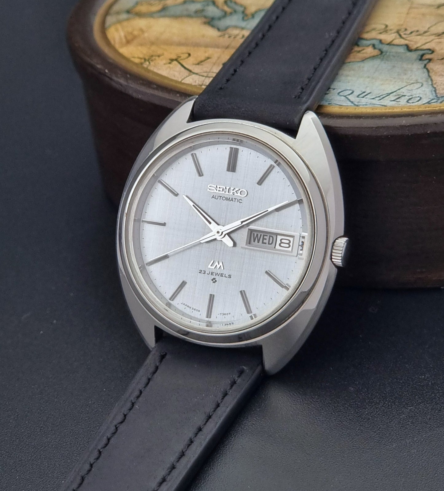 Vintage Seiko Lord Matic 5606-7150 watch with black leather strap on a dark background crown view