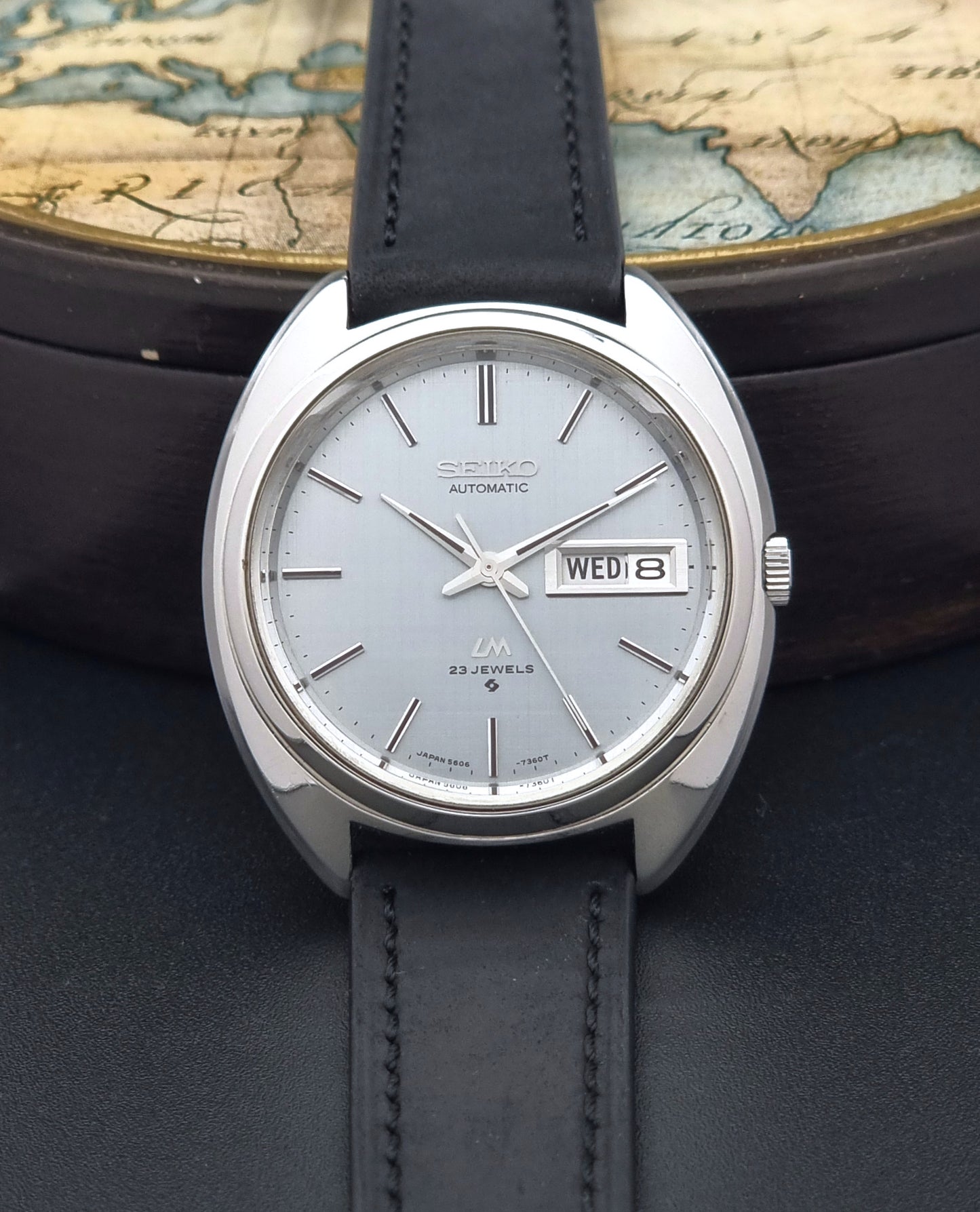 Vintage Seiko Lord Matic 5606-7150 watch with black leather strap on a dark background front view