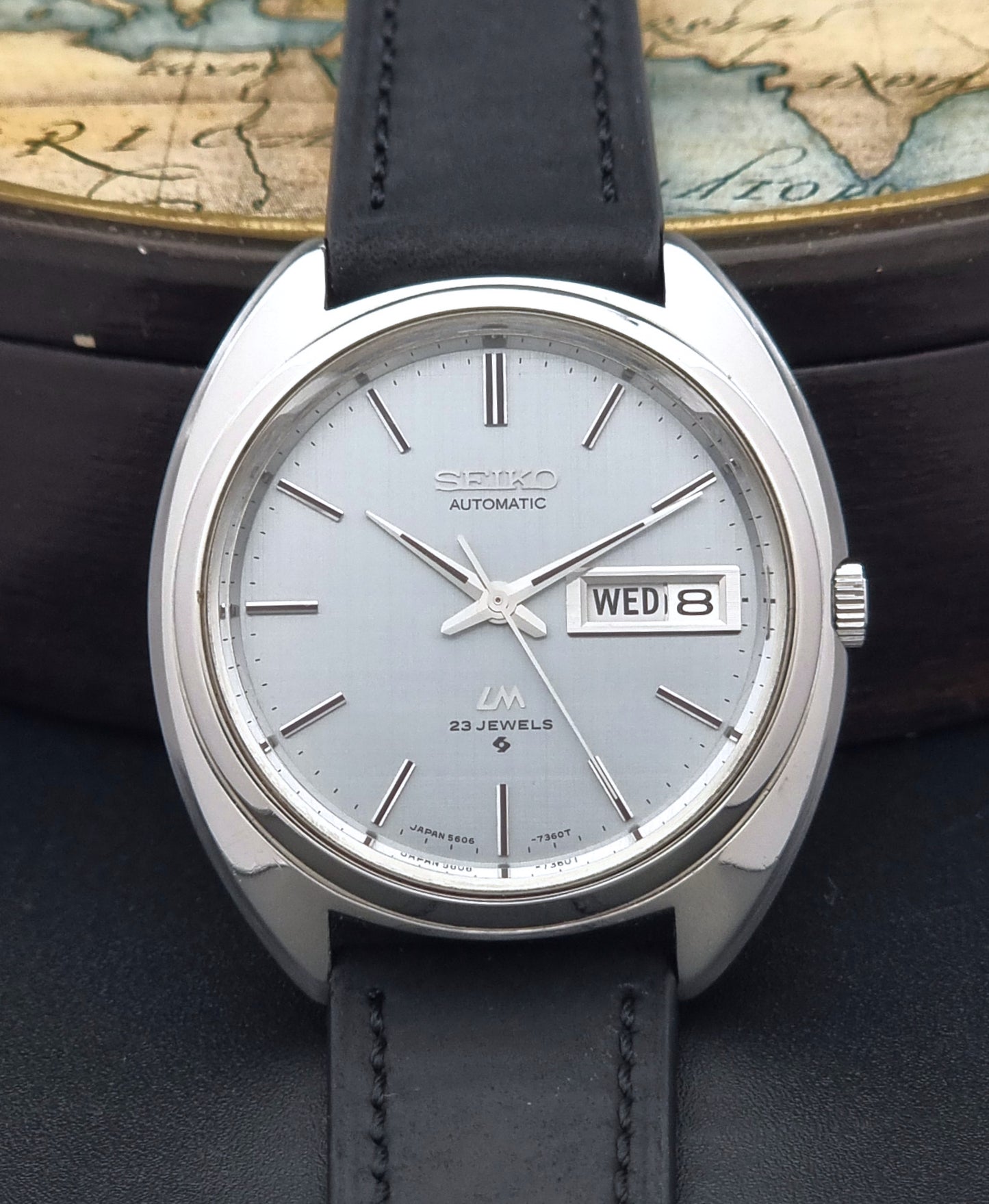 Vintage Seiko Lord Matic 5606-7150 watch with black leather strap on a dark background front close up dial