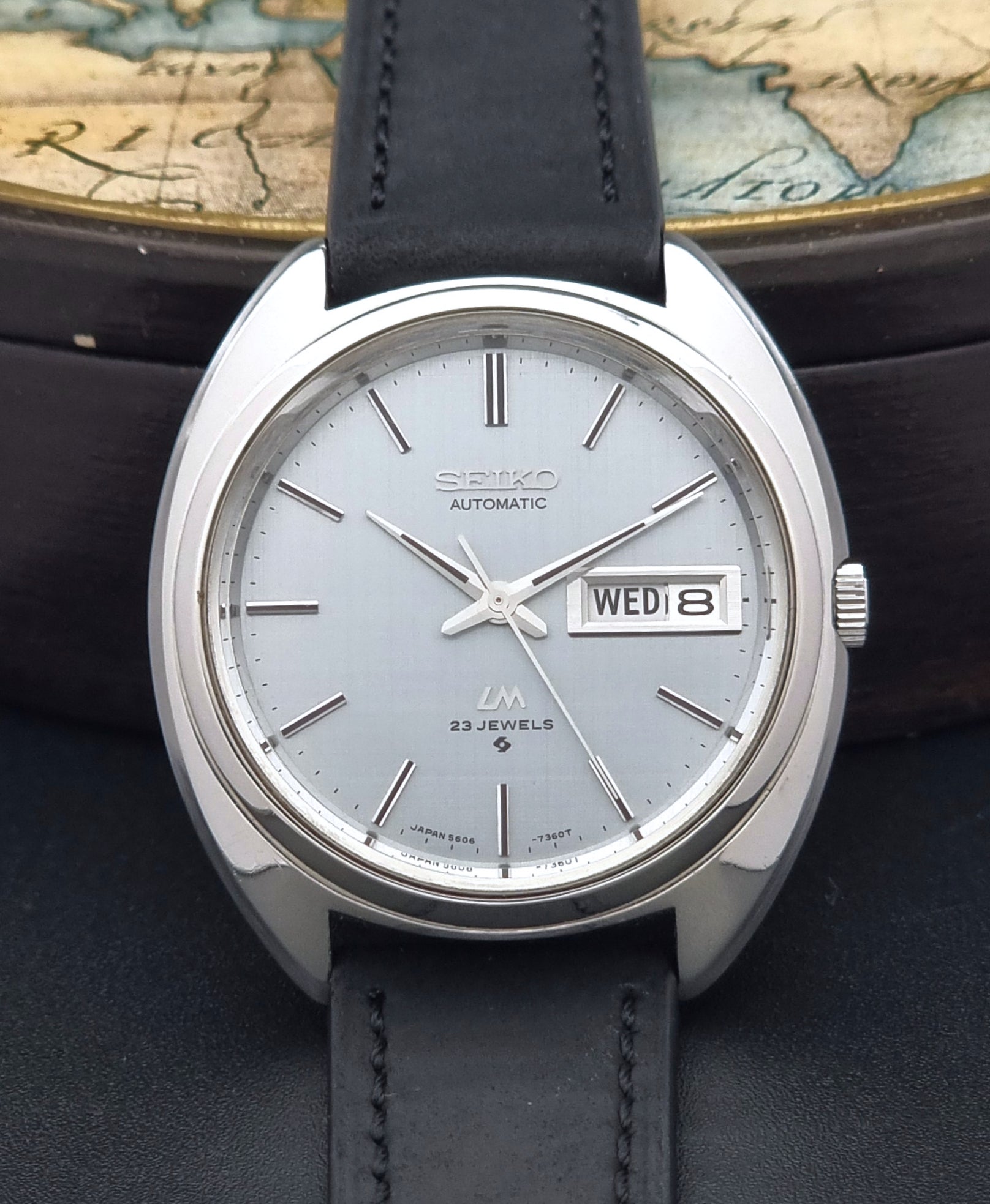 Vintage Seiko Lord Matic 5606-7150 watch with black leather strap on a dark background front close up dial