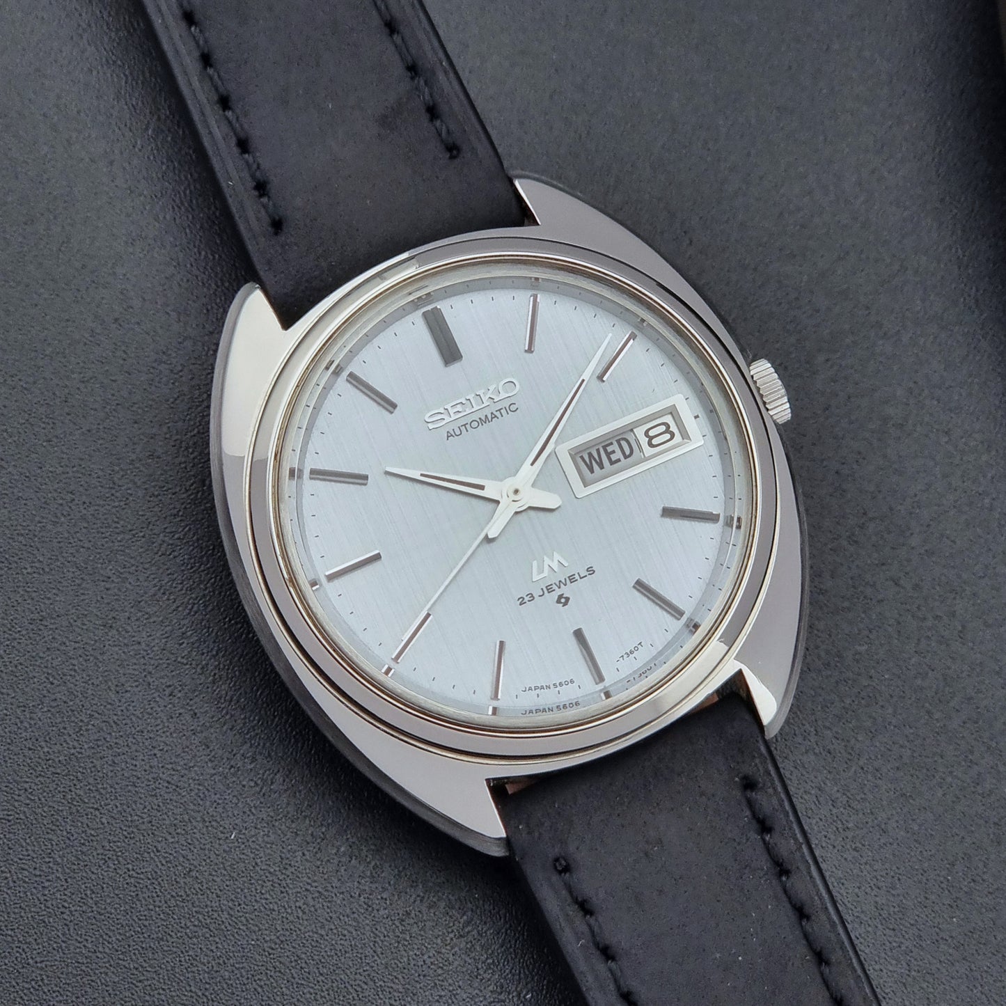 Vintage Seiko Lord Matic 5606-7150 watch with black leather strap on a dark background close up dial