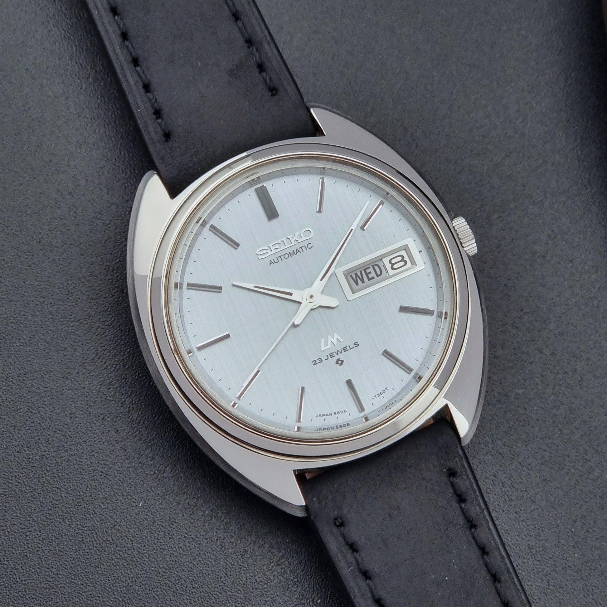 Vintage Seiko Lord Matic 5606-7150 watch with black leather strap on a dark background close up dial