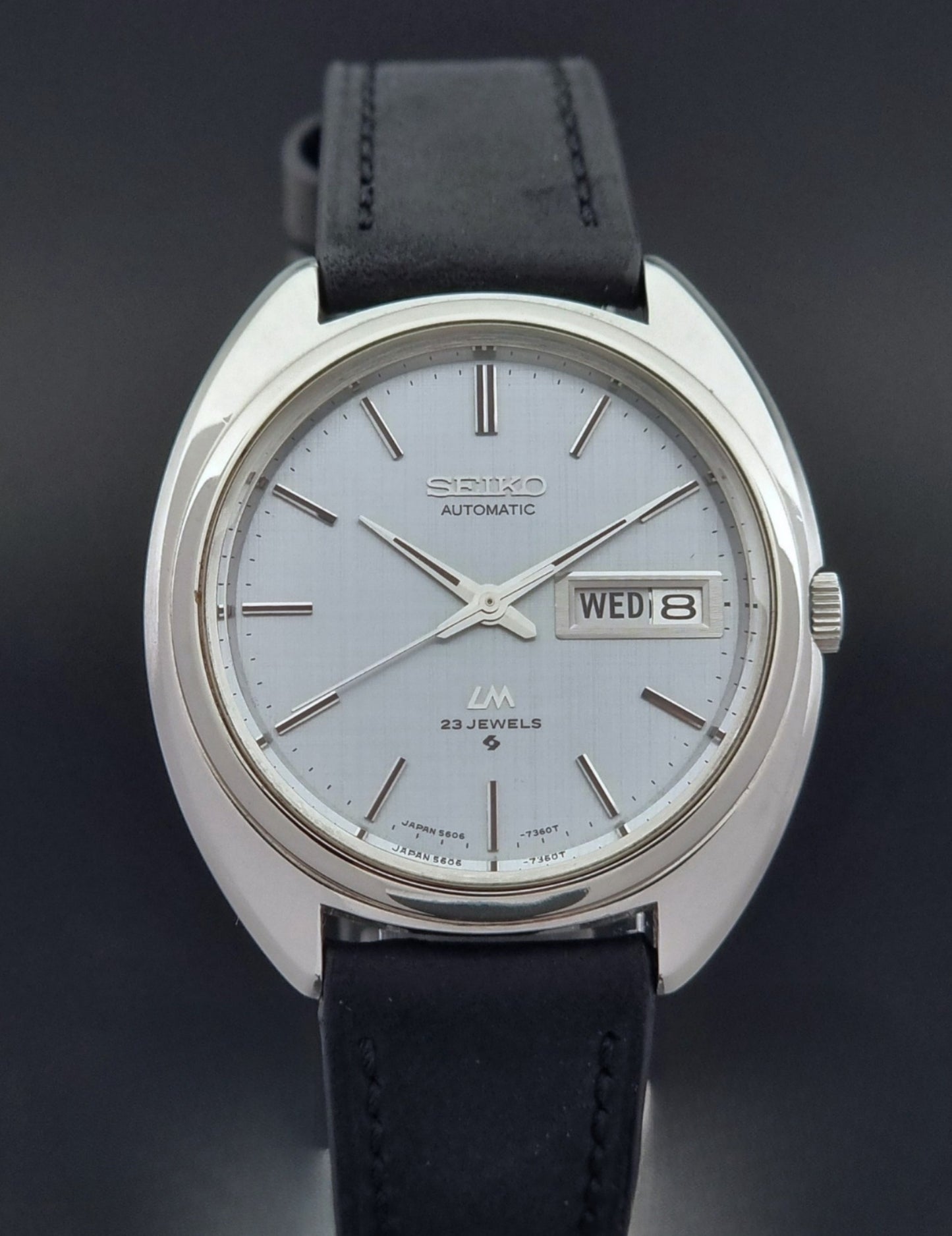 Vintage Seiko Lord Matic 5606-7150 watch with black leather strap on a dark background close up