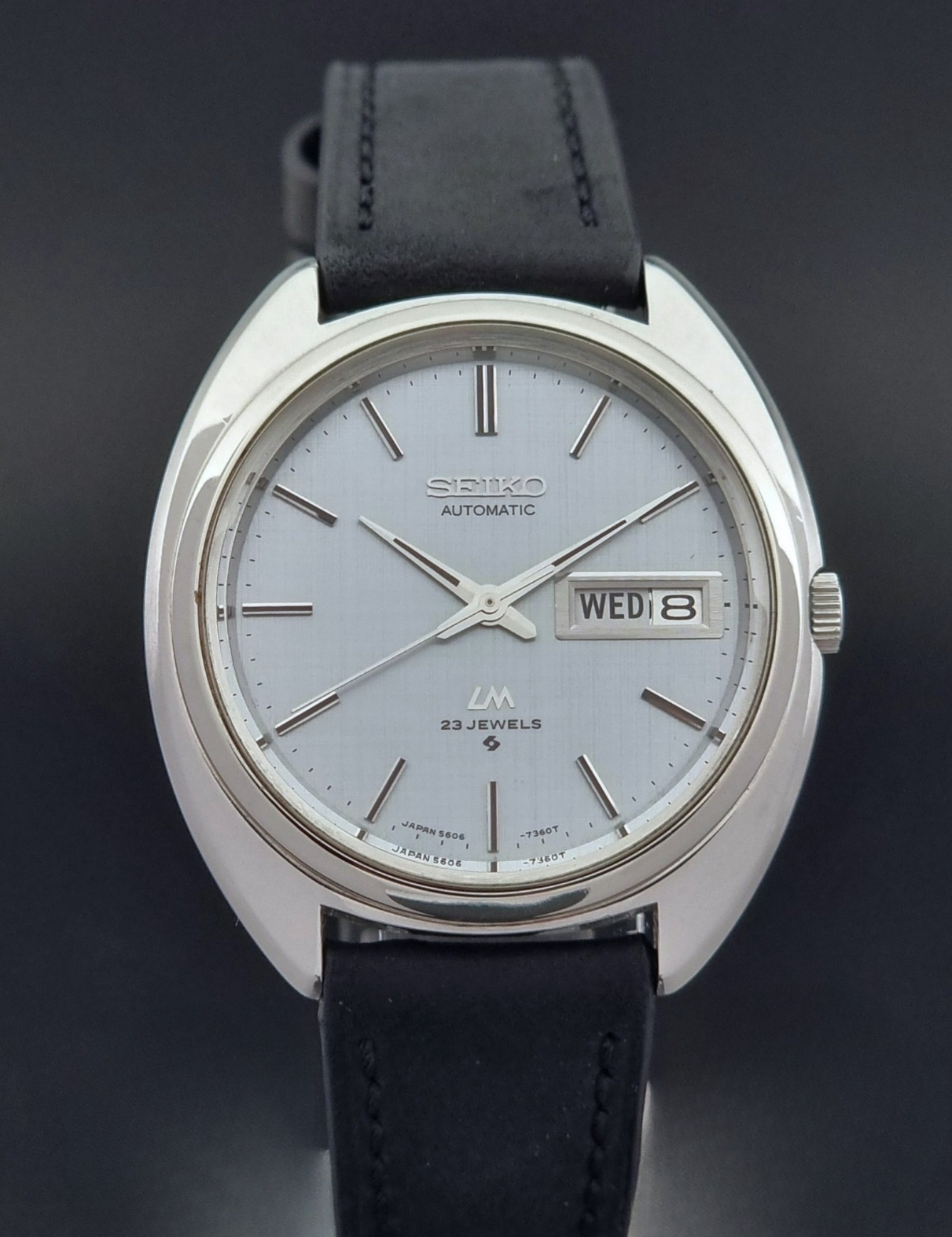 Vintage Seiko Lord Matic 5606-7150 watch with black leather strap on a dark background close up