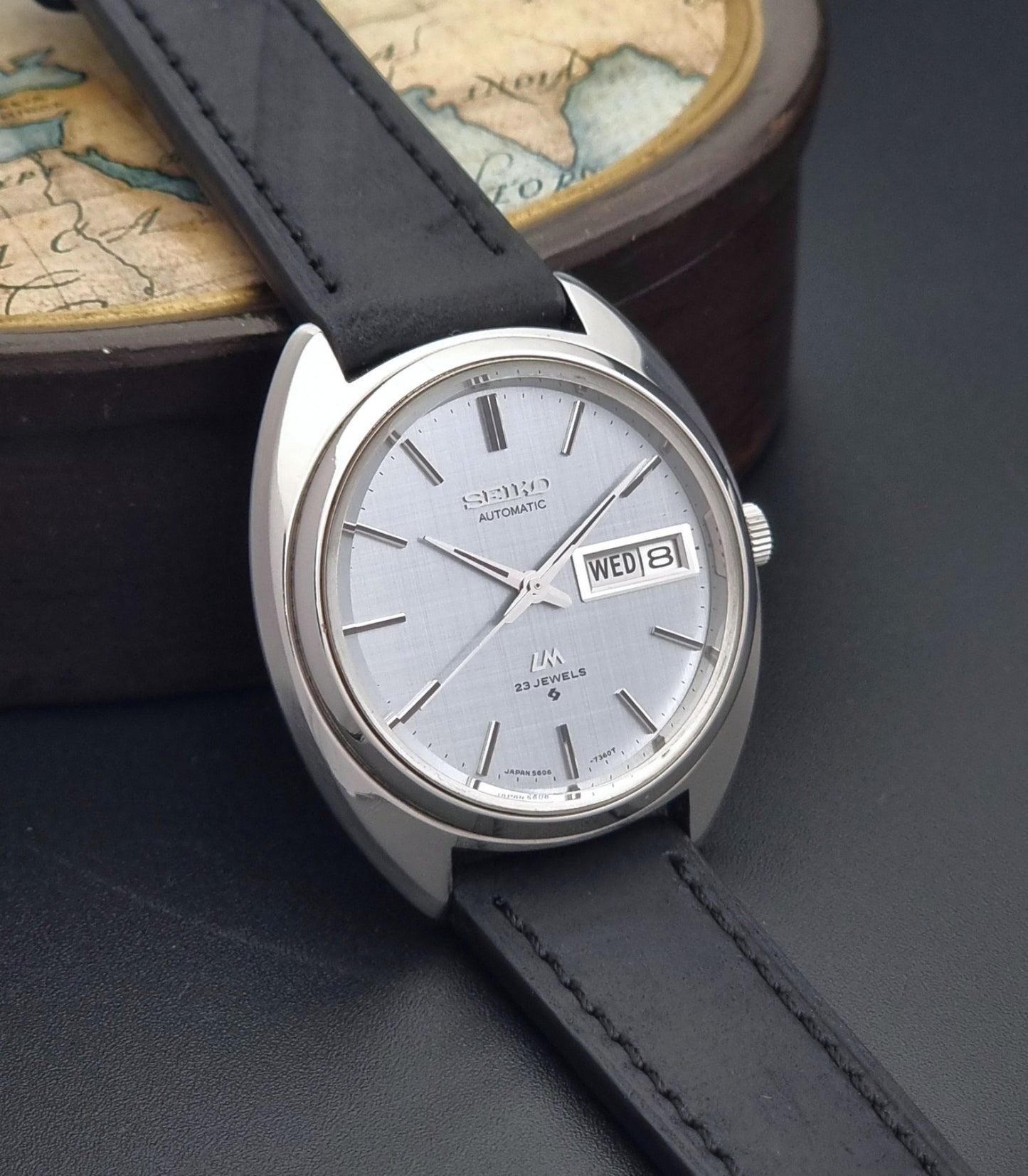 Vintage Seiko Lord Matic 5606-7150 watch with black leather strap on a dark background side view