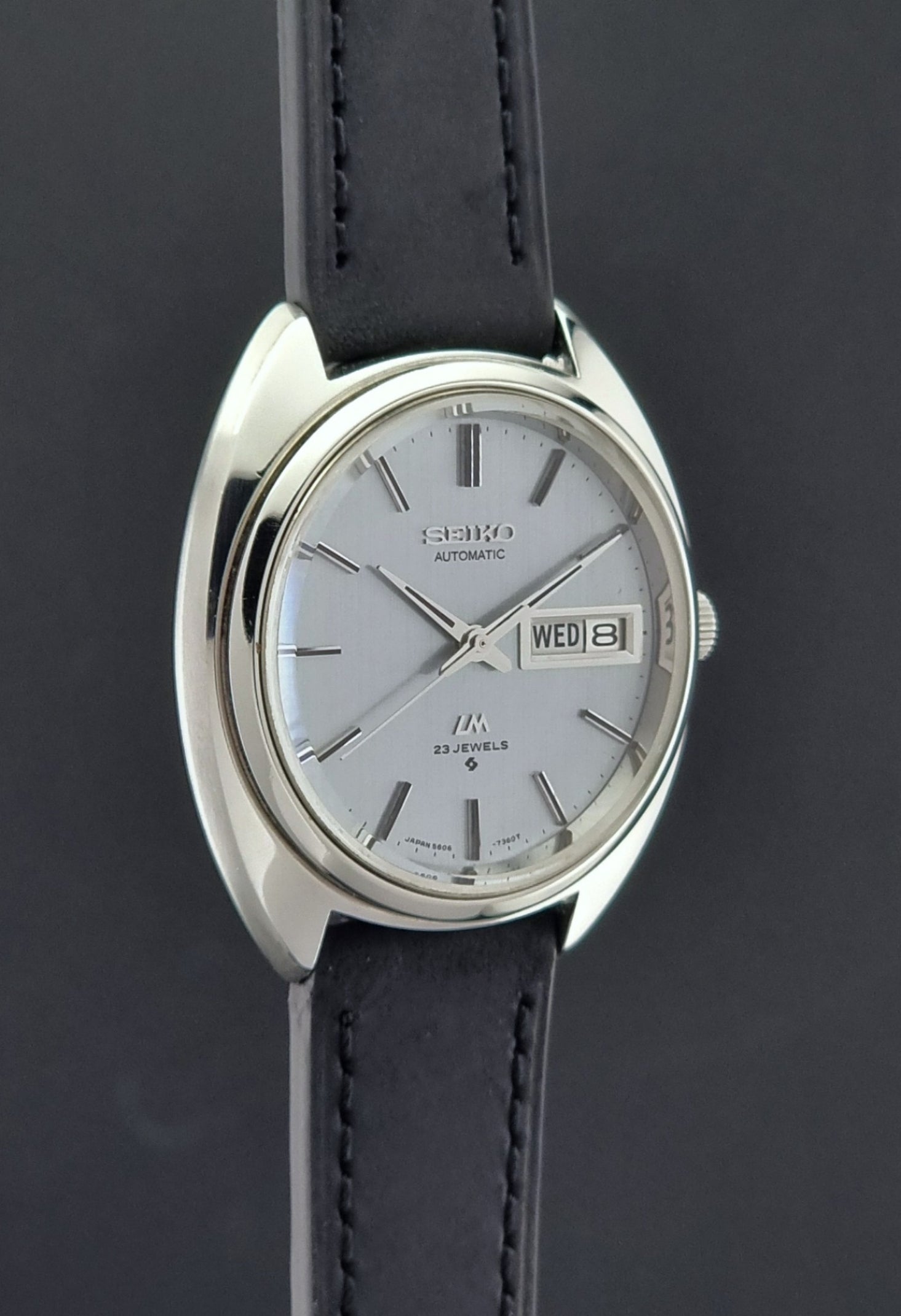 Vintage Seiko Lord Matic 5606-7150 watch with black leather strap on a dark background side profile