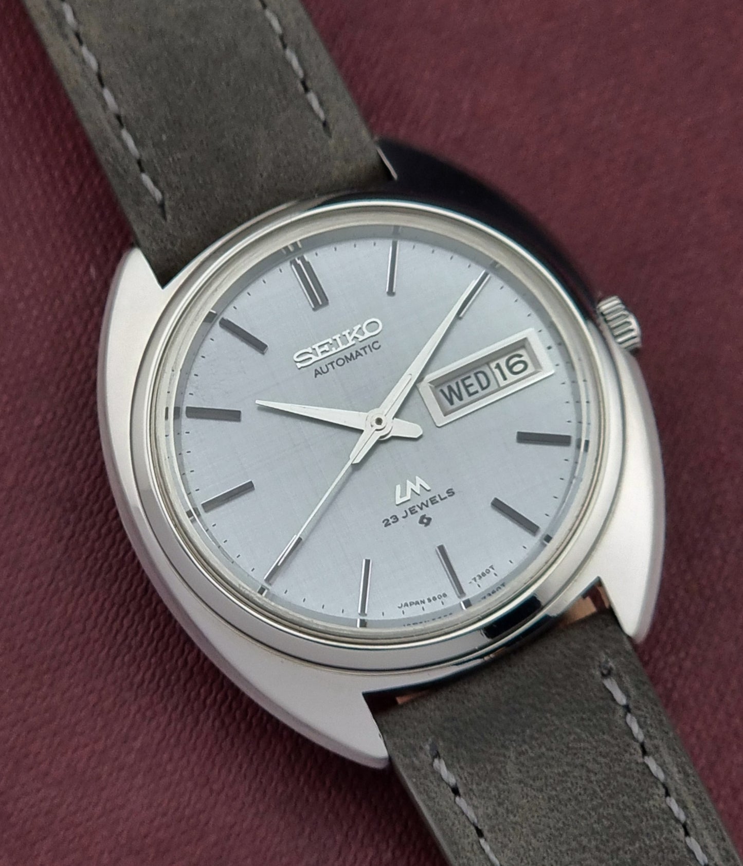 Seiko watch with gray leather strap on a maroon background