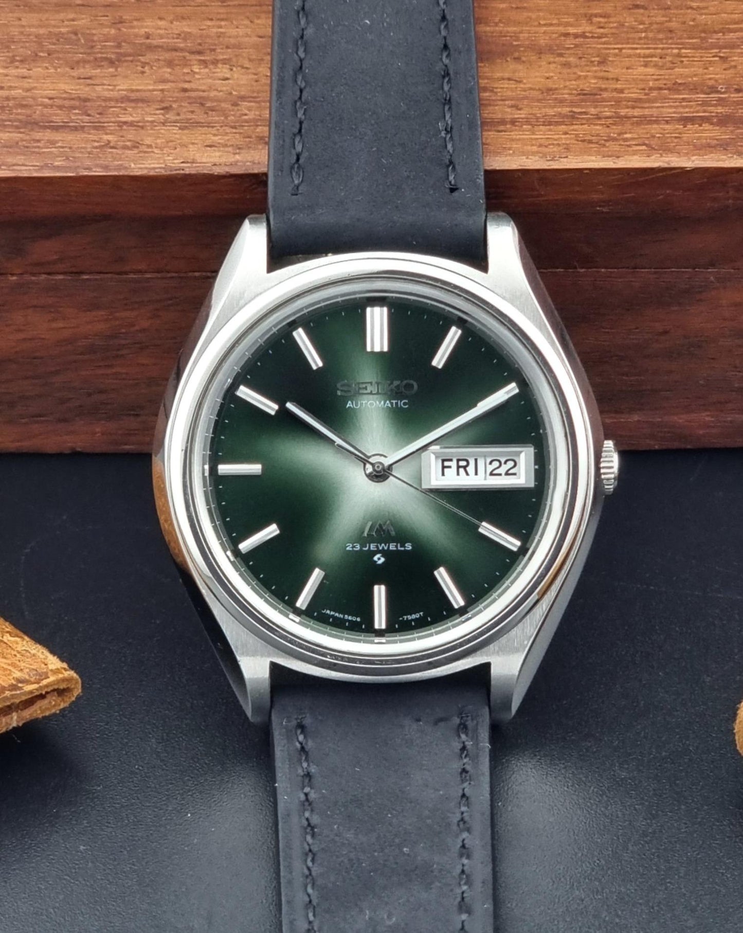 Front view of a Vintage Seiko Lord Matic watch with green face and dark leather strap on a wooden surface