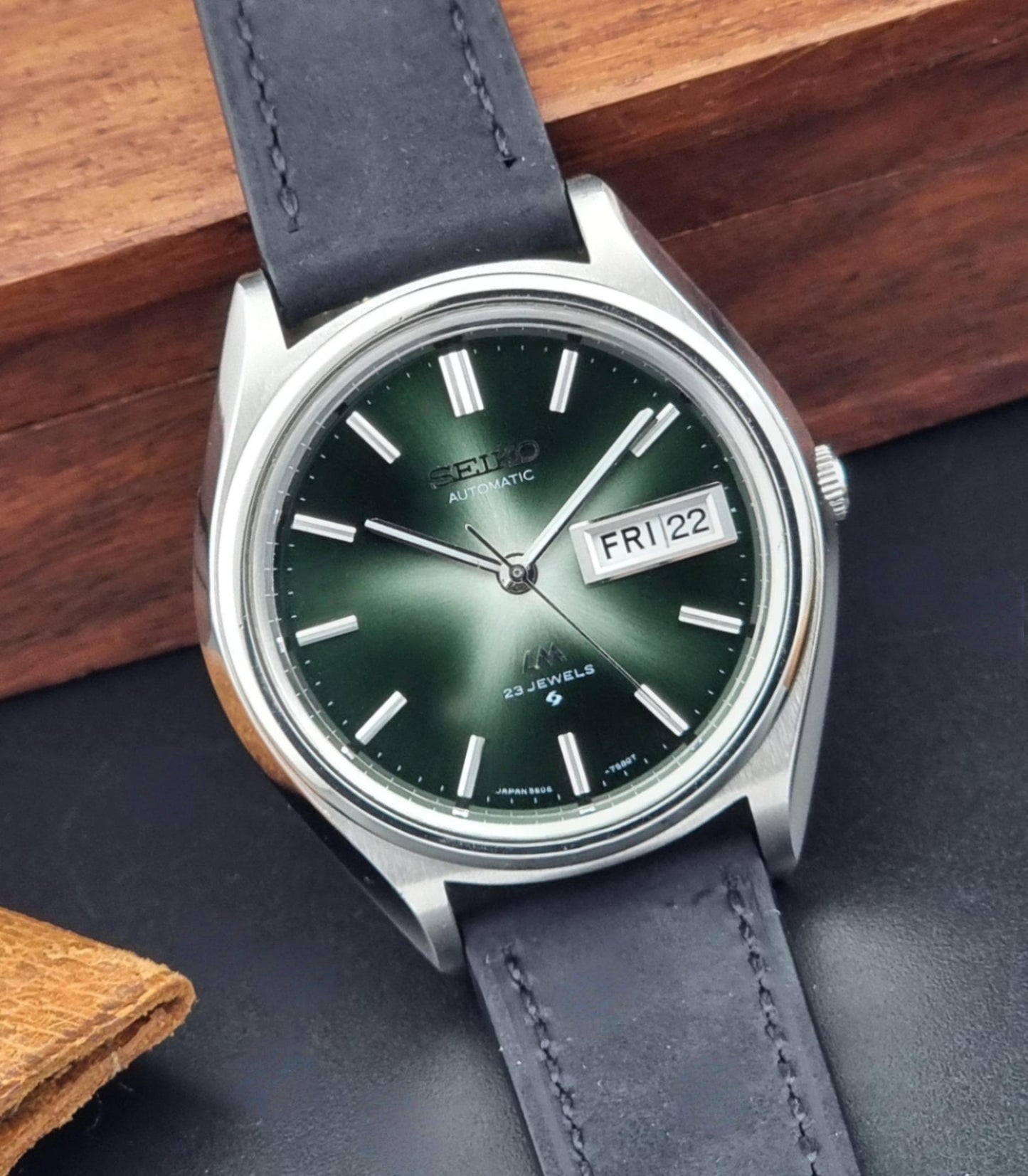 Vintage Seiko Lord Matic watch with green dial and dark leather strap on a wooden surface