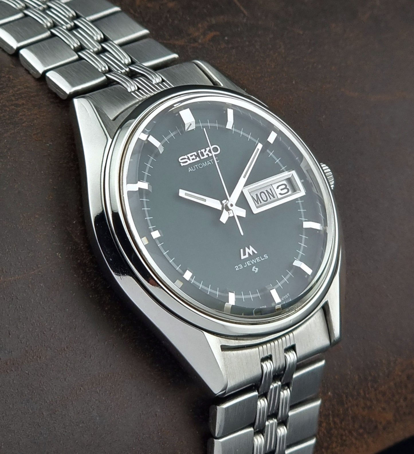 Silver Seiko watch with a dark face on a brown leather background