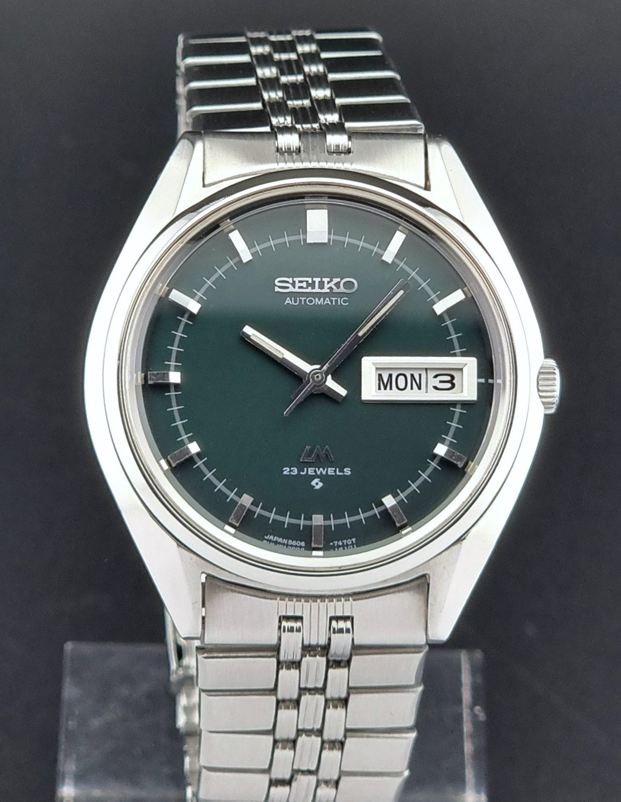 Seiko watch with green dial and silver metal band on a black background
