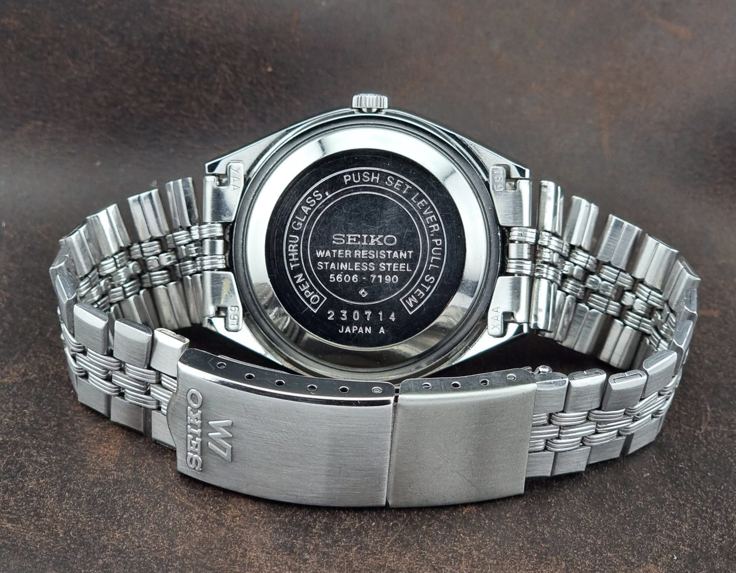 Silver Seiko watch case back on a dark brown background