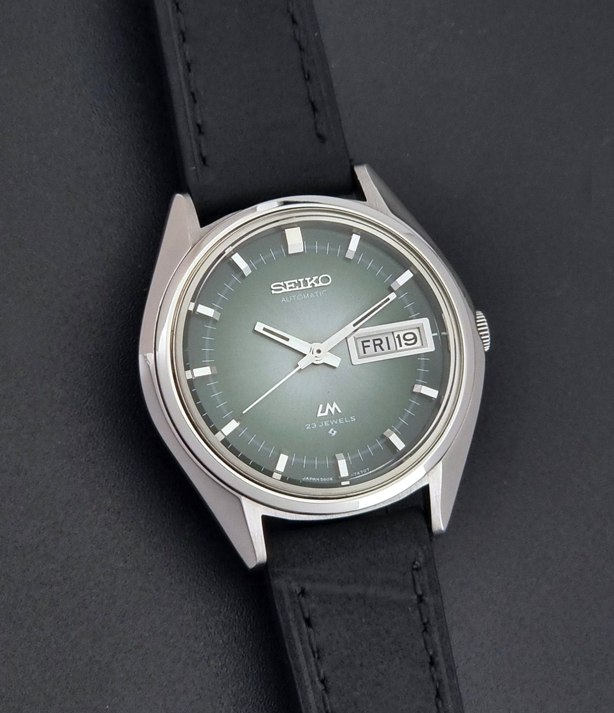 Vintage Seiko LordMatic 5606-7191 watch with a black leather strap on a dark gray background front view