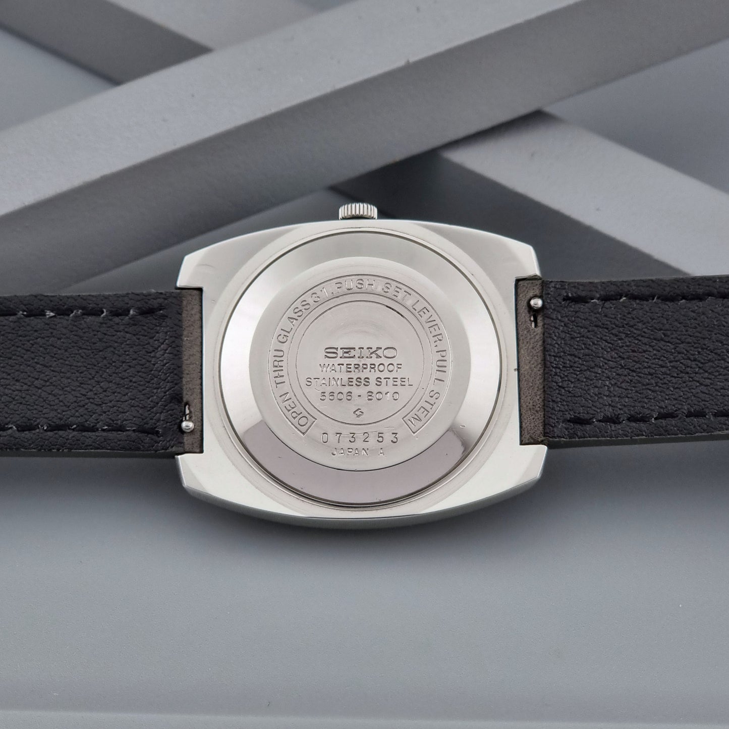 Vintage Seiko Lord Matic 5606-8010 watch with grey leather strap on a gray background case back