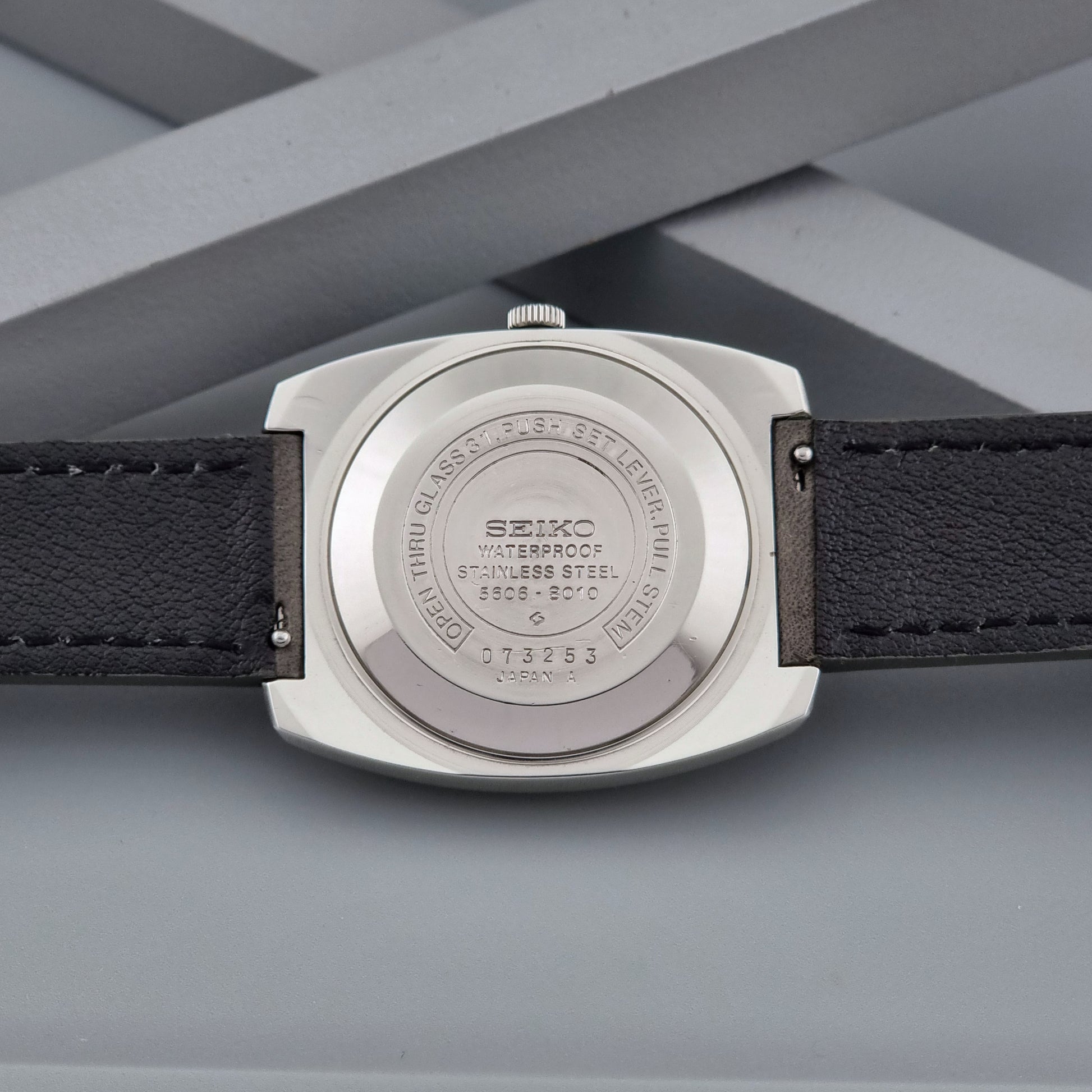 Vintage Seiko Lord Matic 5606-8010 watch with grey leather strap on a gray background case back