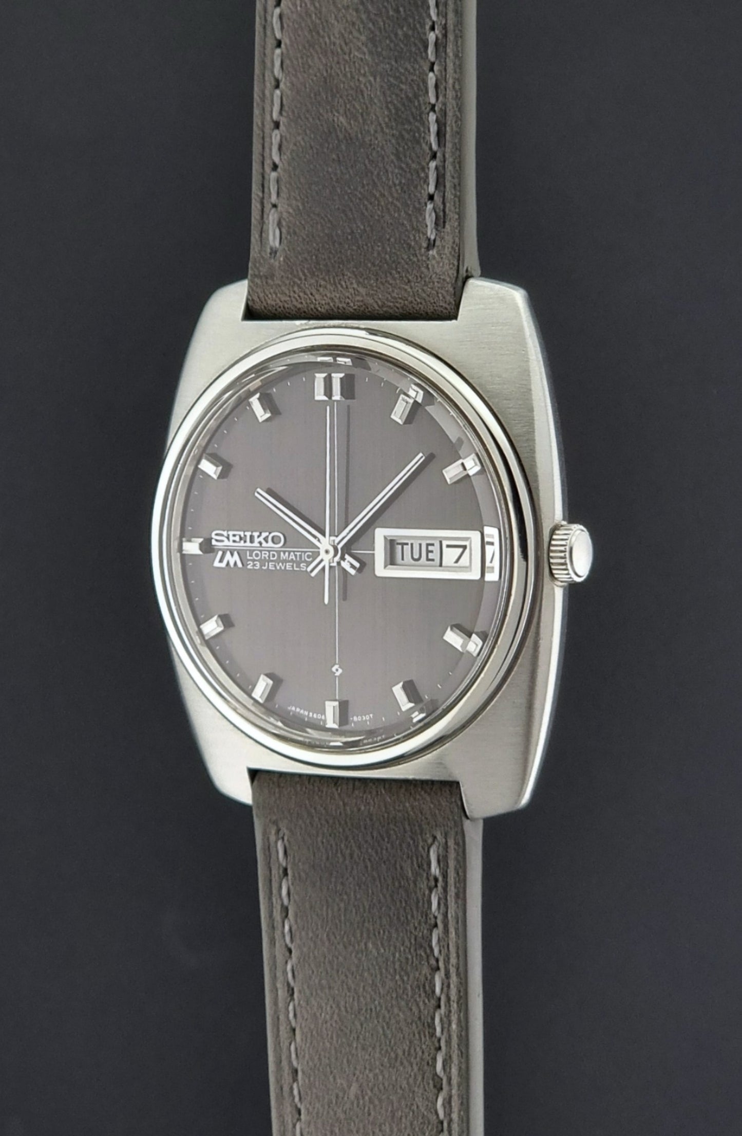 Vintage Seiko Lord Matic 5606-8010 watch with grey leather strap on a gray background crown side profile