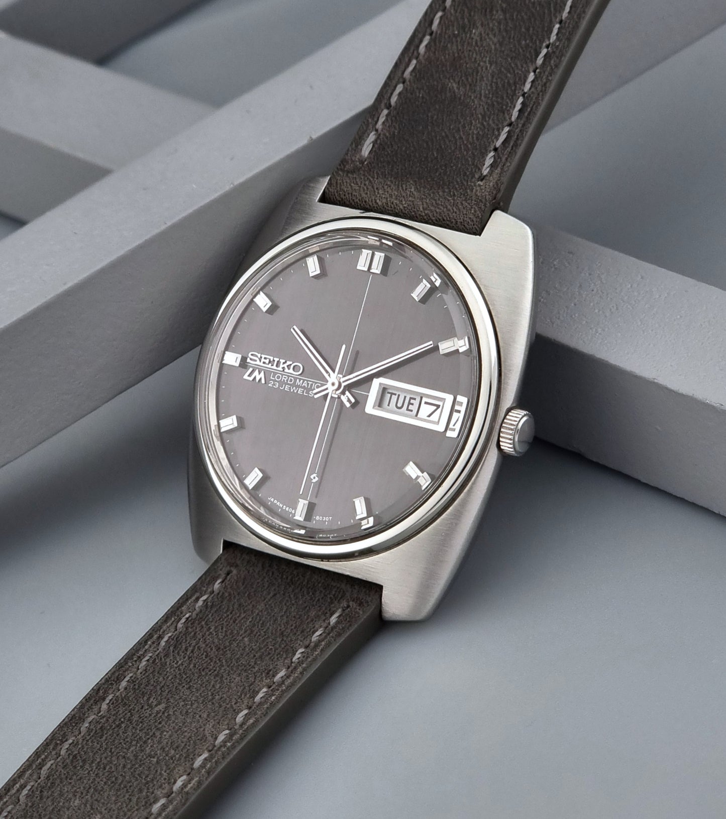 Vintage Seiko Lord Matic 5606-8010 watch with grey leather strap on a gray background crown side view
