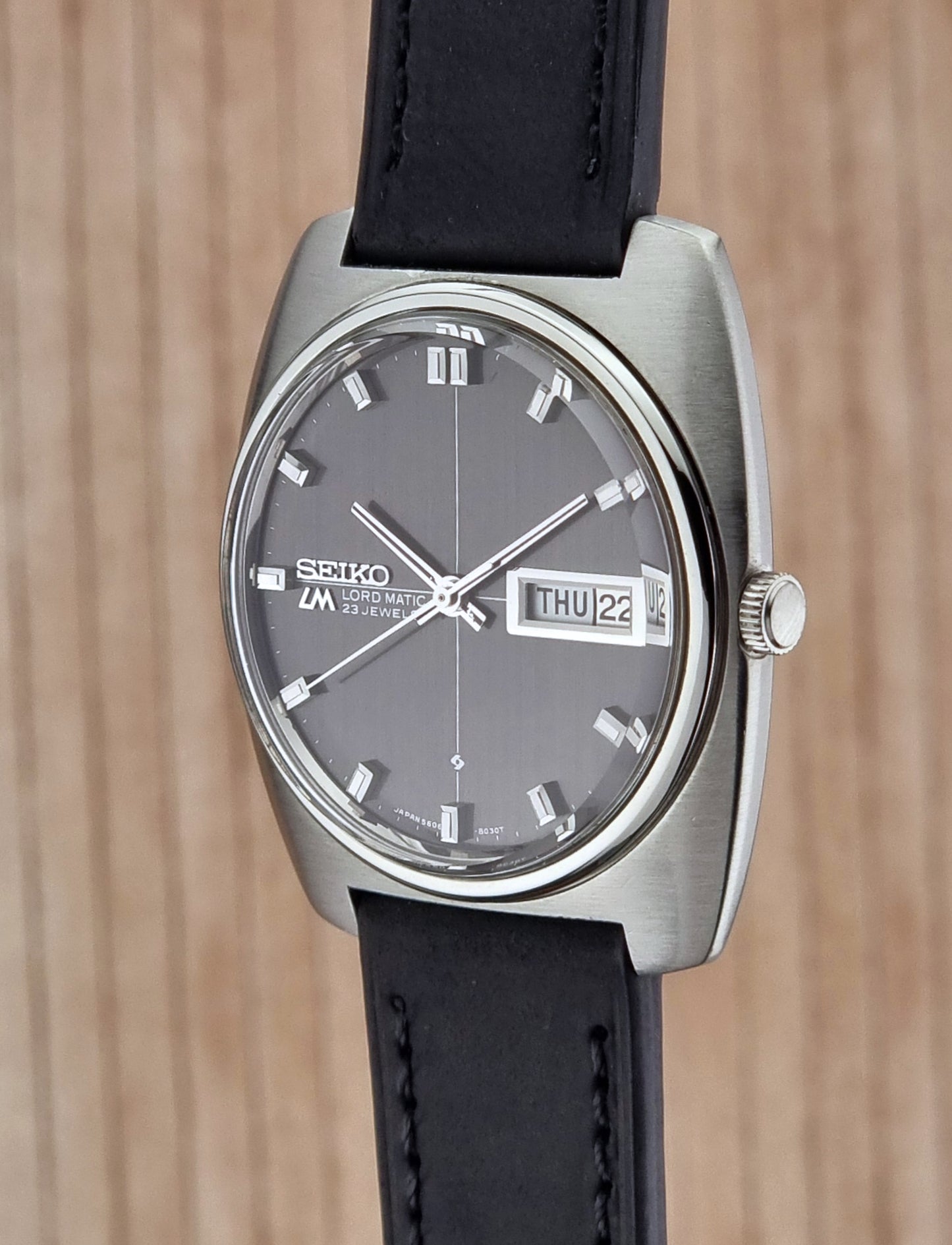 Side view of a Seiko watch with black leather strap on a wooden background