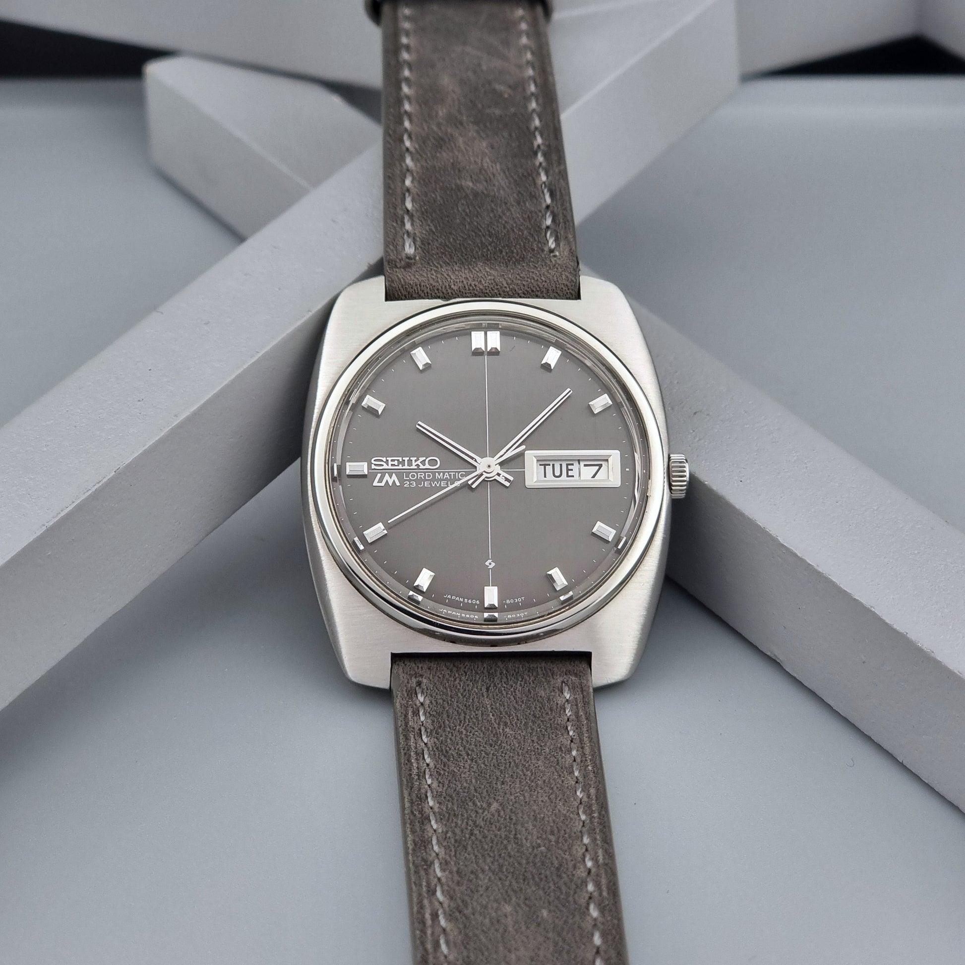 Vintage Seiko Lord Matic 5606-8010 watch with grey leather strap on a gray background front view