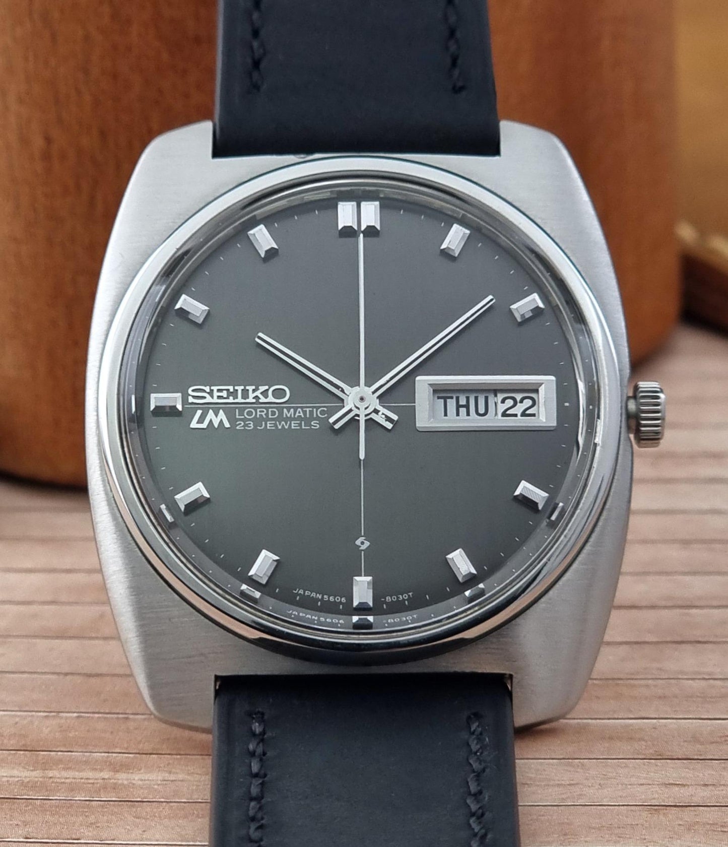 Front view of a Seiko Lord Matic watch with black leather strap on a wooden surface