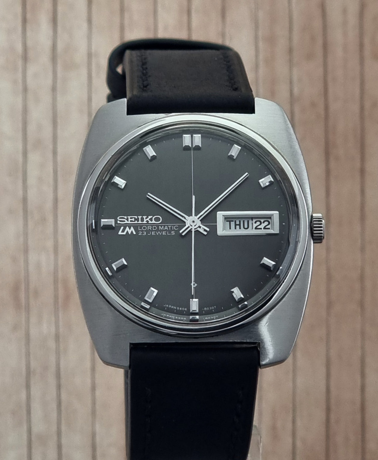 Seiko Lord Matic watch with black strap and dark face on wooden surface