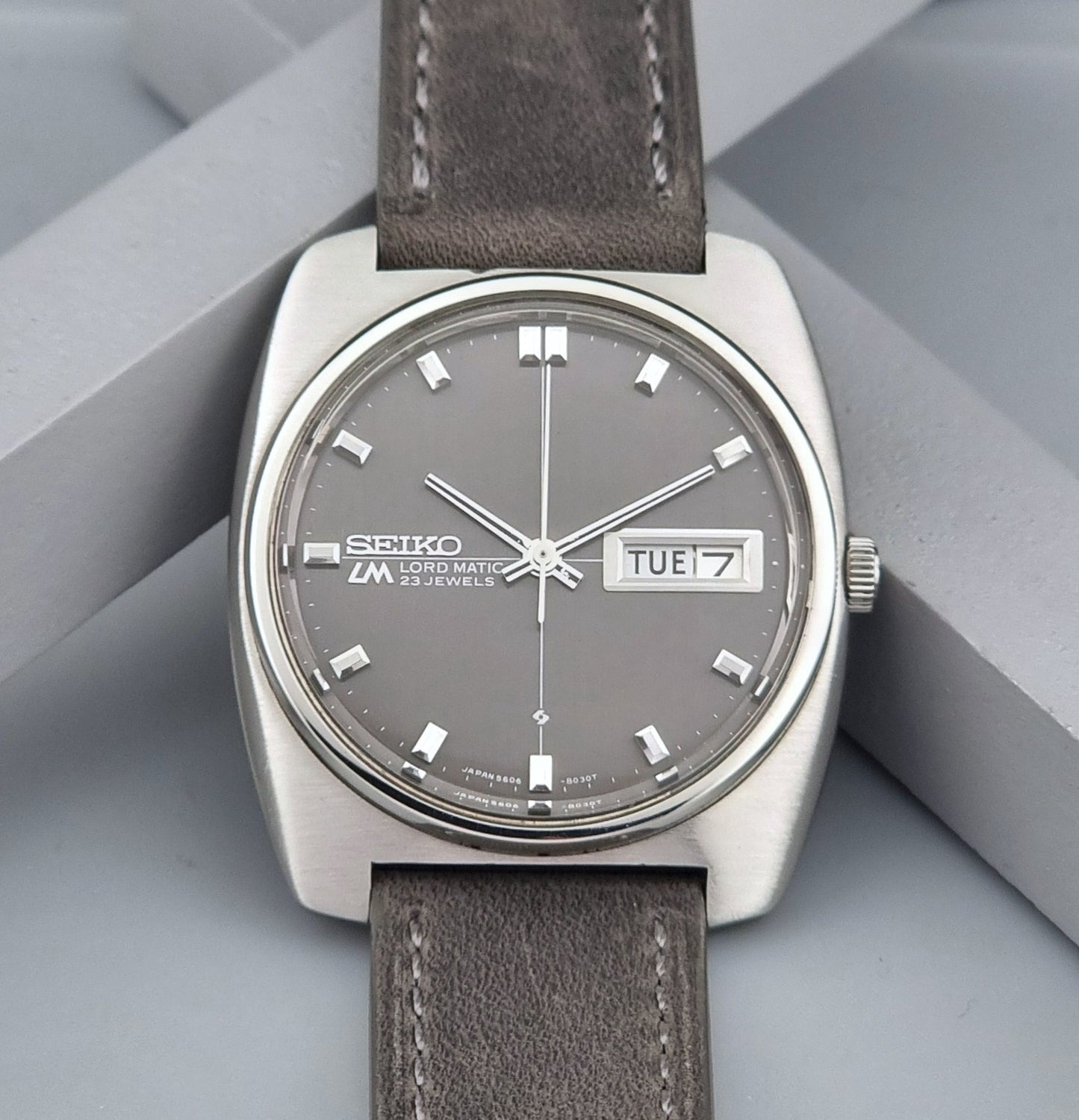Vintage Seiko Lord Matic 5606-8010 watch with grey leather strap on a gray background close up of dial