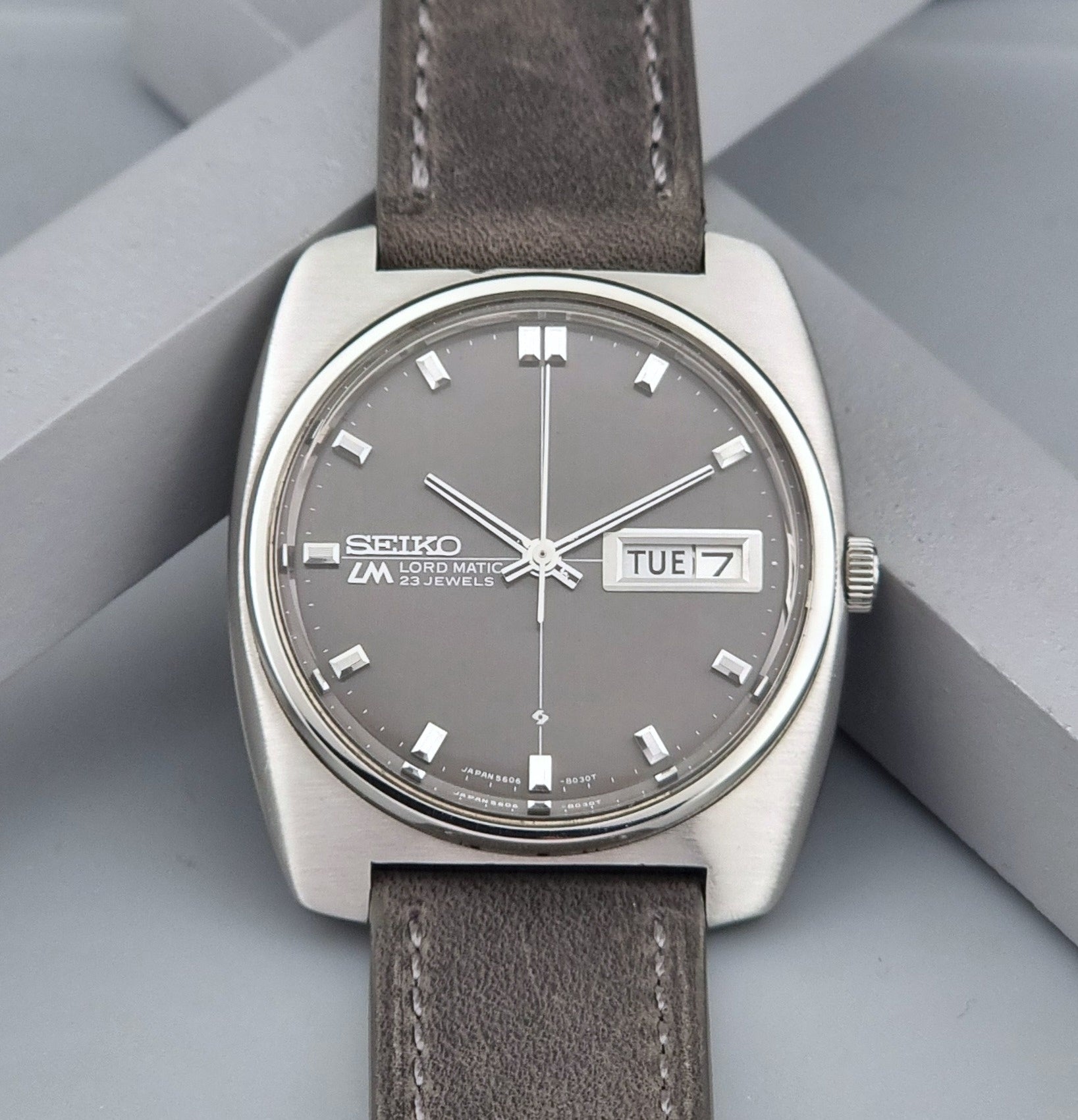 Vintage Seiko Lord Matic 5606-8010 watch with grey leather strap on a gray background close up of dial