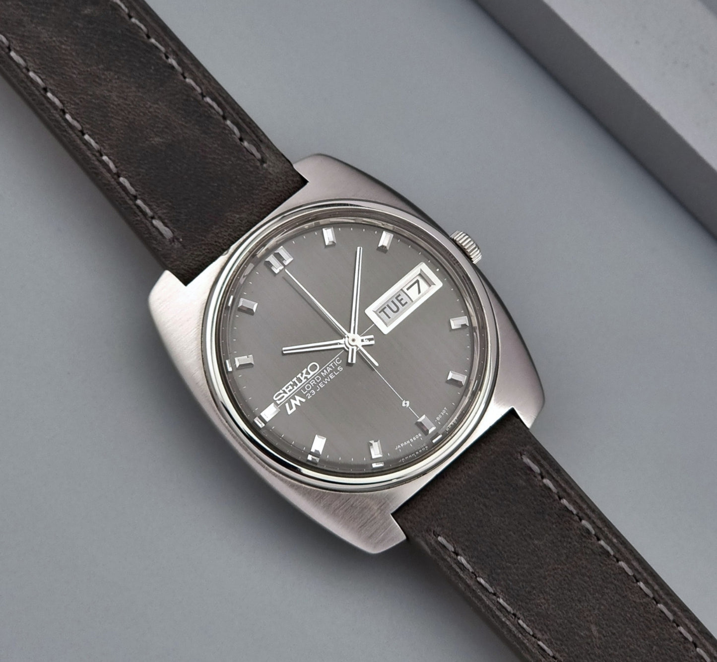 Vintage Seiko Lord Matic 5606-8010 watch with grey leather strap on a gray background