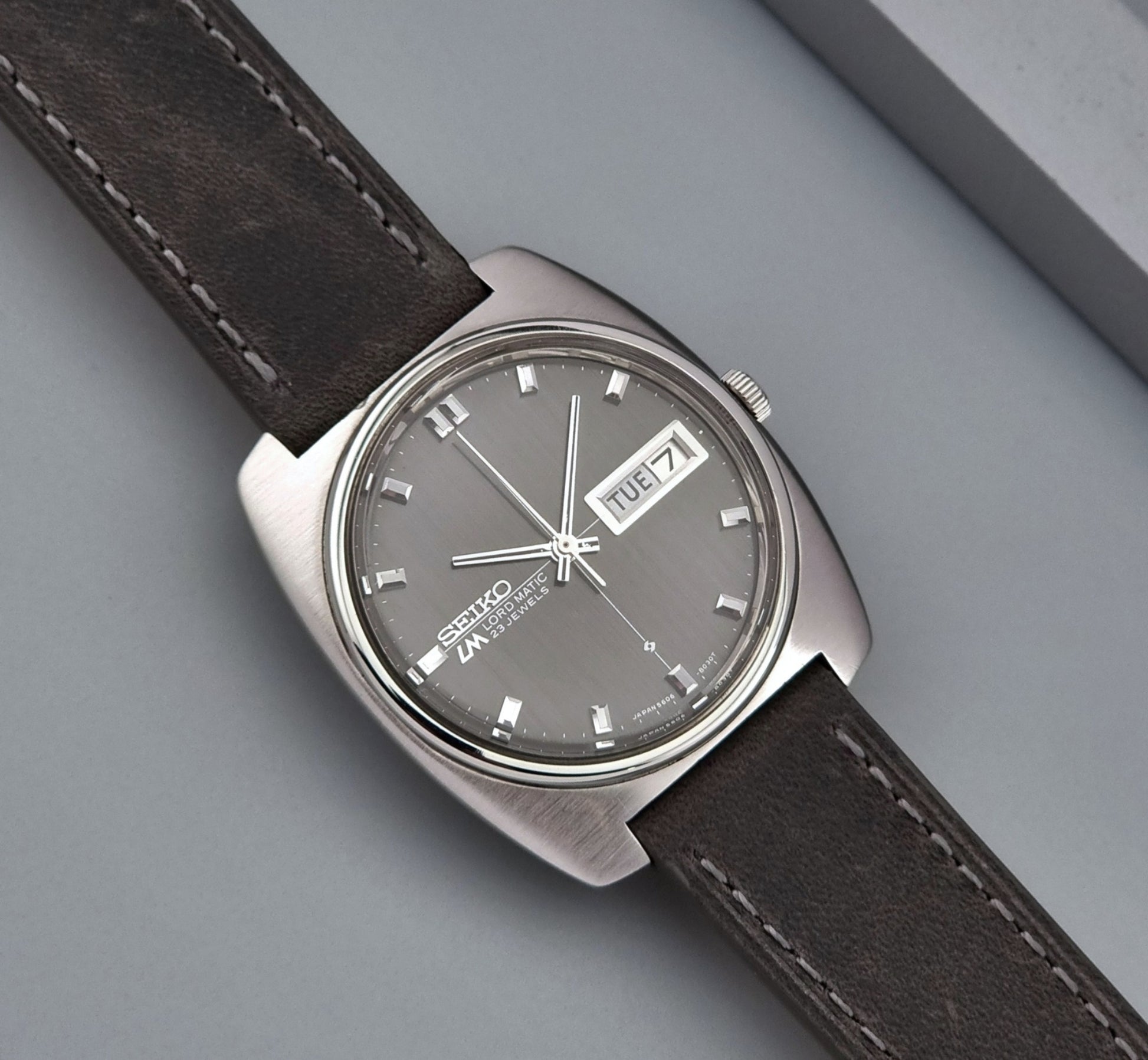 Vintage Seiko Lord Matic 5606-8010 watch with grey leather strap on a gray background