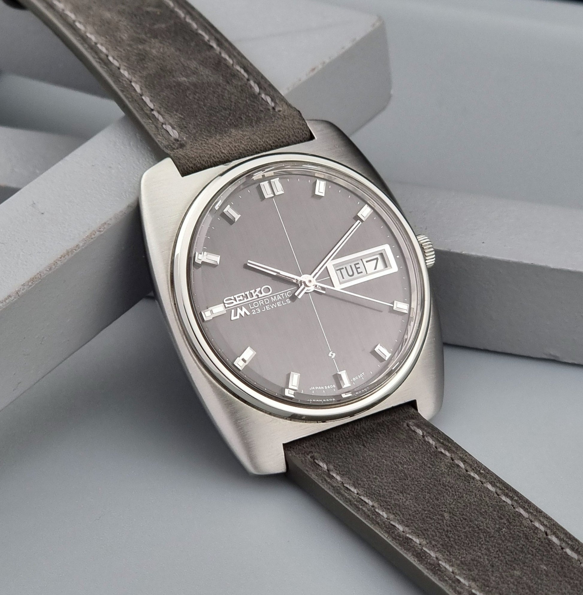 Vintage Seiko Lord Matic 5606-8010 watch with grey leather strap on a gray background side view